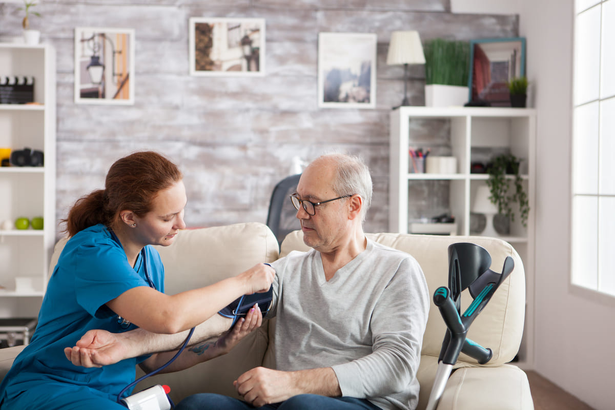 Female nurse attaching digital device old mans arm check blood pressure
